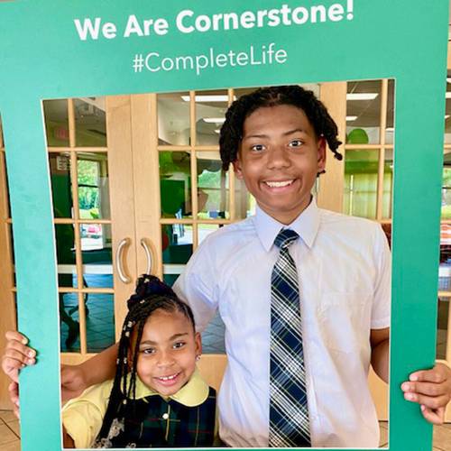 Two students smile and pose with a Cornerstone Schools prop frame